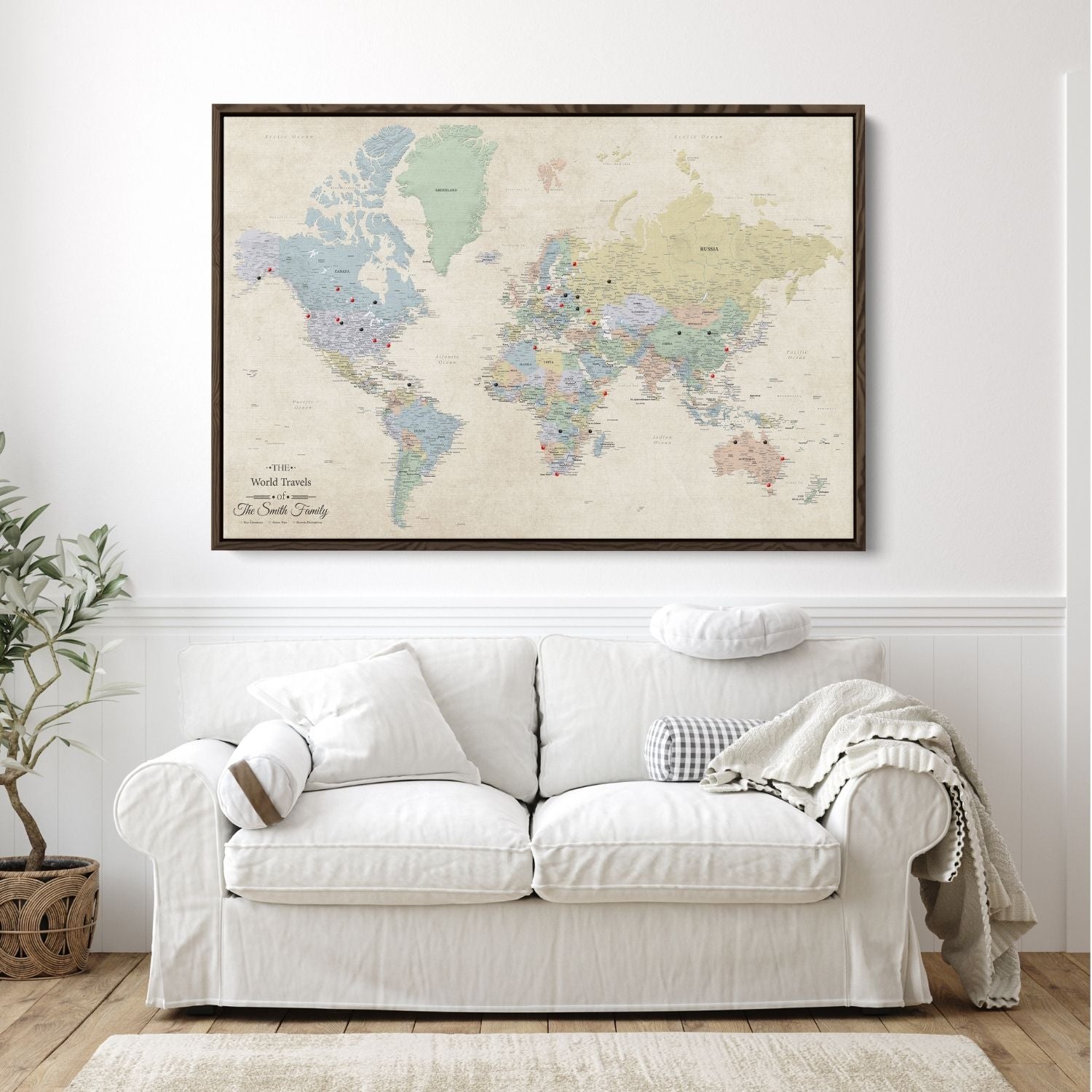 Personalized Sandy Dreams world travel map canvas in brown float frame with red and black push pins hung above white sofa