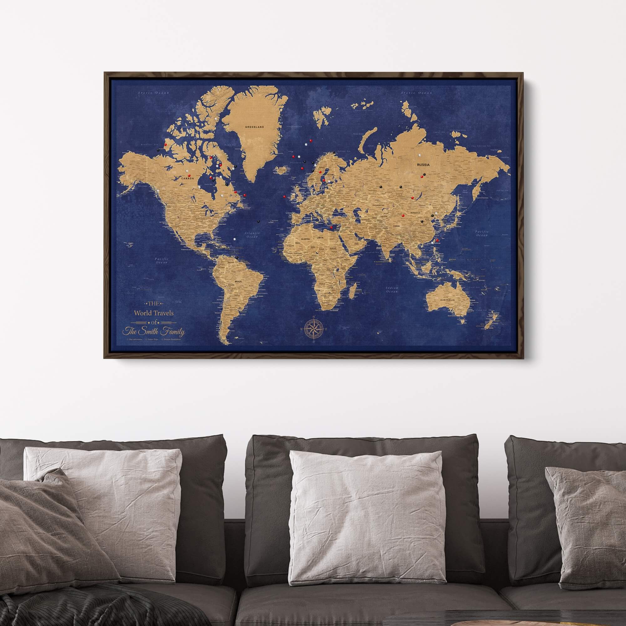 Personalized gold and navy world travel map with push pins displayed on wall above gray sofa