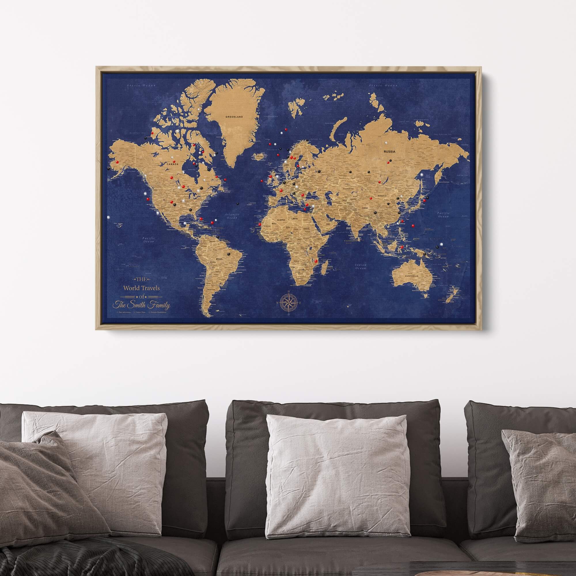 Personalized gold and navy world travel map with push pins displayed in wooden frame above gray sofa