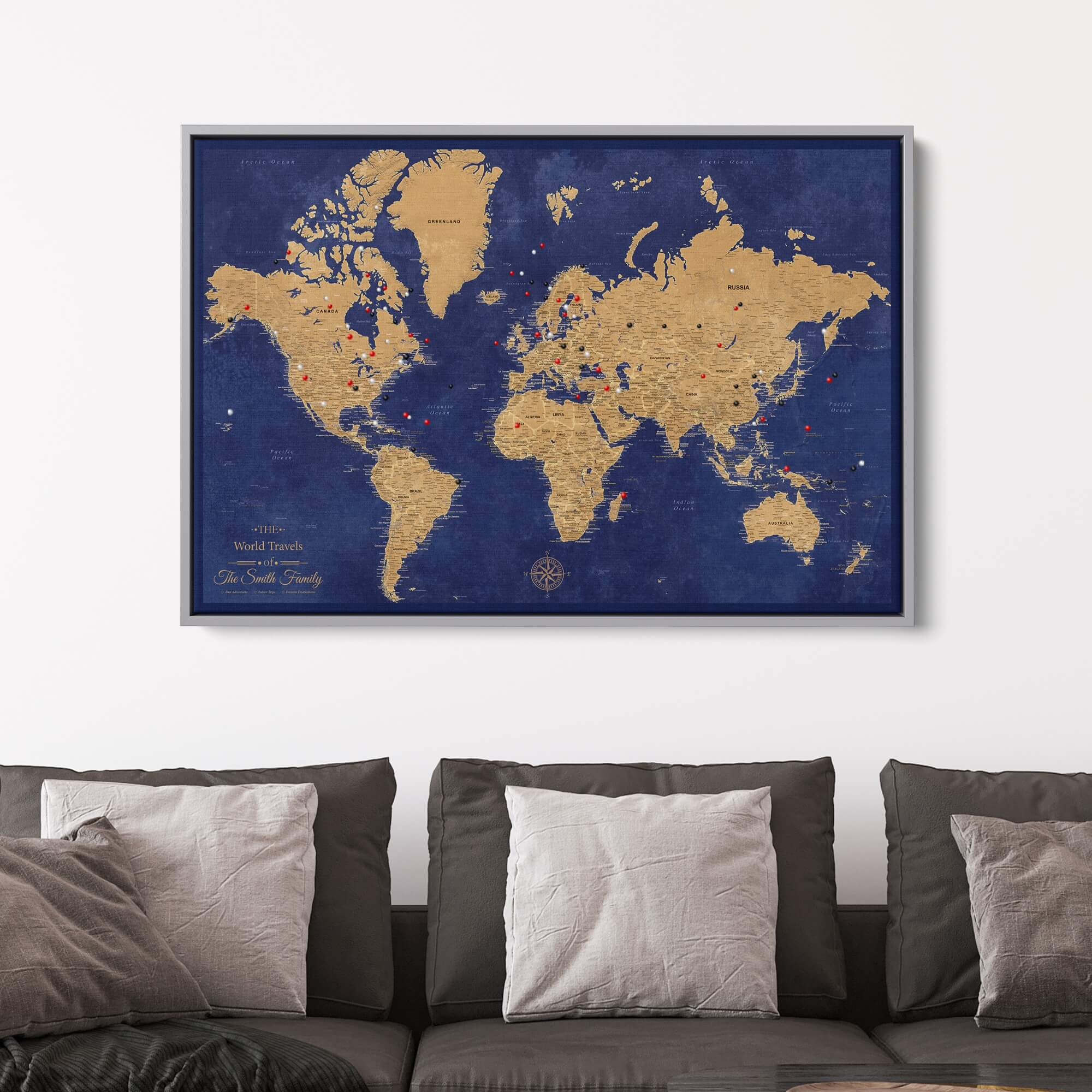 Framed canvas gold and navy world travel map with push pins displayed above gray sofa