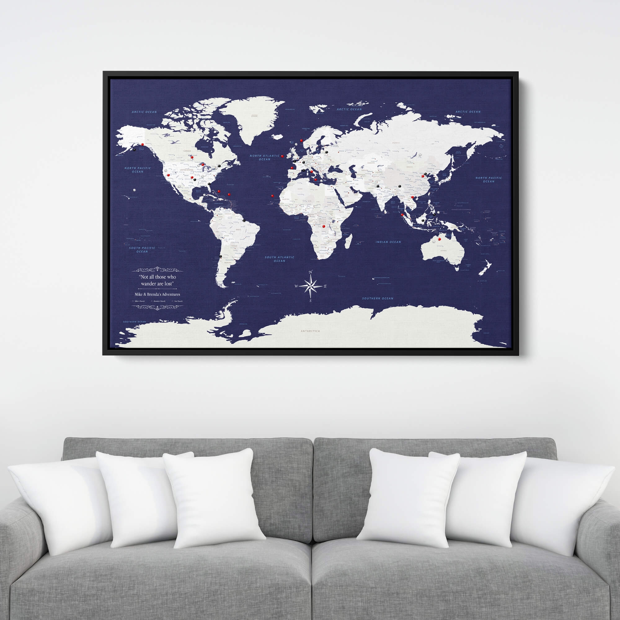 Navy Explorers world travel map canvas with red push pins in black frame above gray sofa