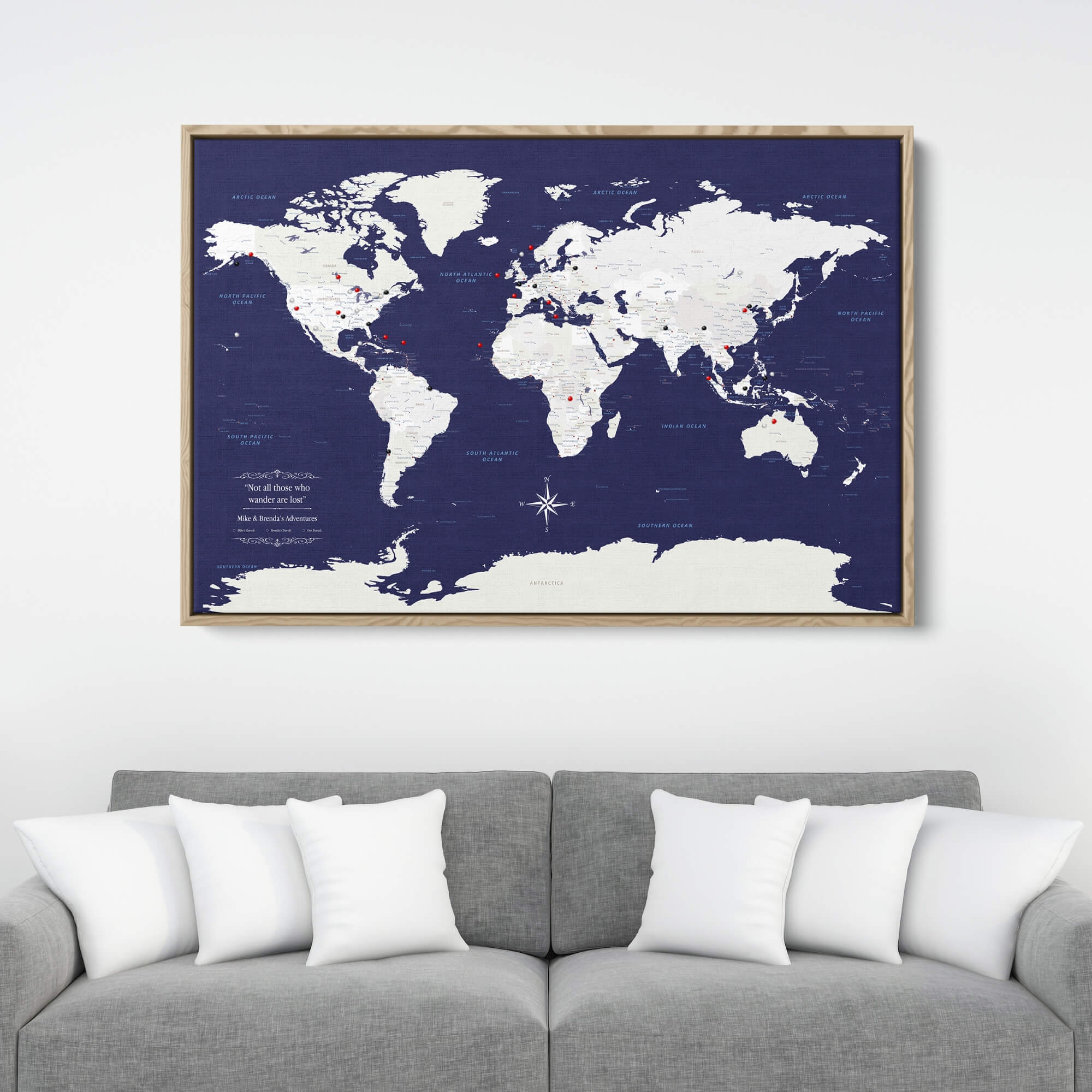 Navy Explorers world travel map canvas with red push pins in wooden frame above gray sofa