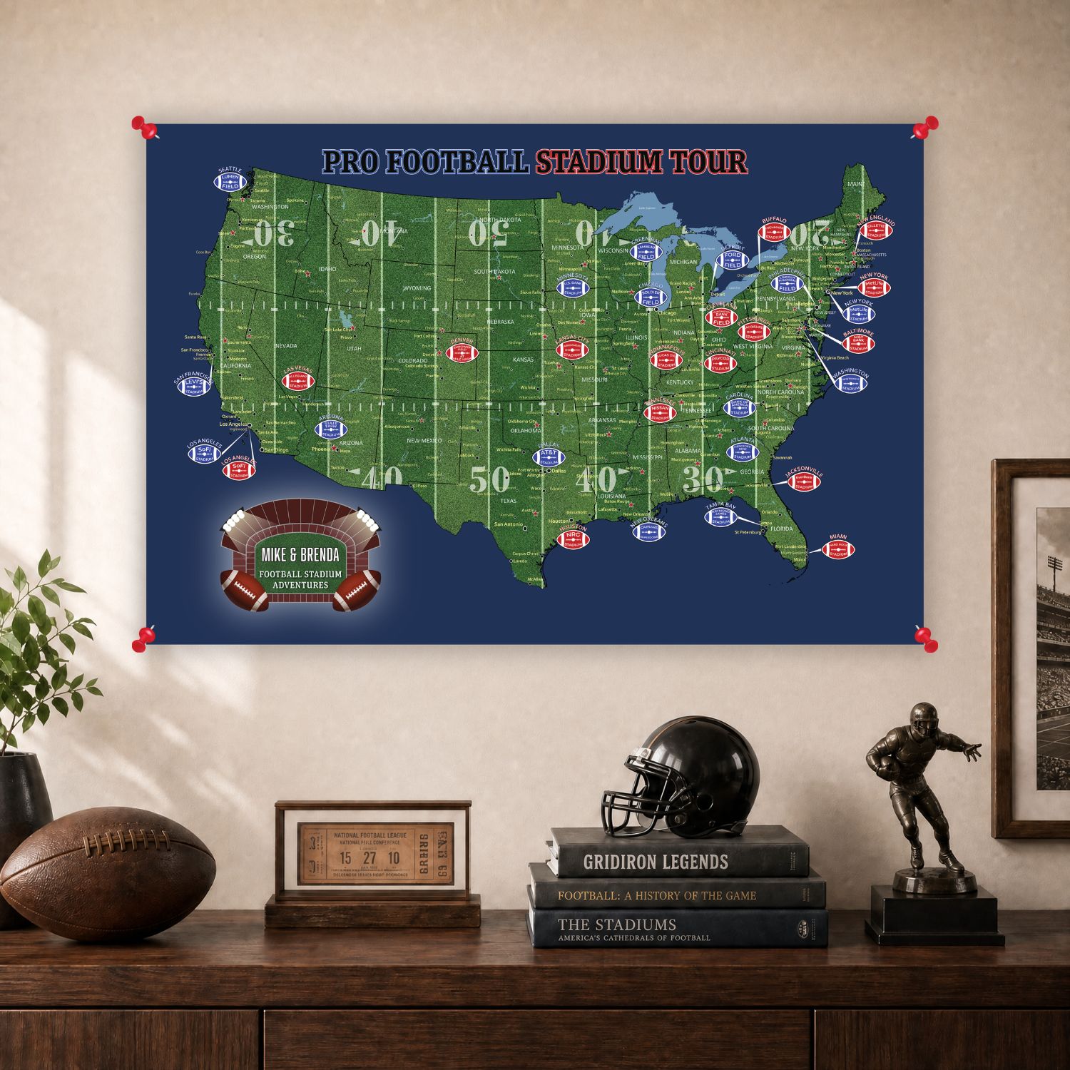 A framed Pro Football Stadium Tour map poster hanging on a wall above a wooden console table. The poster shows a green United States map with football field markings on a dark blue background, with red pins holding it in place.