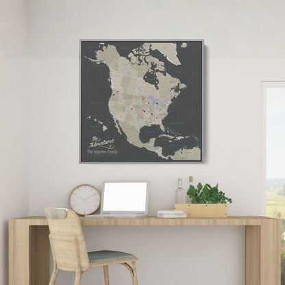 Personalized earth toned North America travel map with push pins in gray frame hung above wooden desk