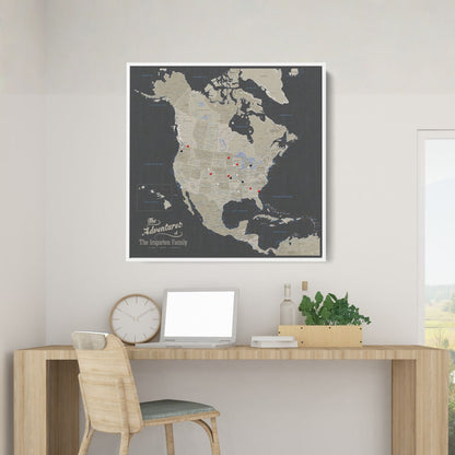 Personalized earth toned North America travel map with push pins in white frame above wooden desk